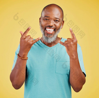 肖像成熟的友好的非洲美国男人。快乐微笑使岩石手手势黄色的工作室背景表达聚会，派对岩石音乐表达式庆祝活动
