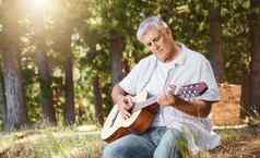 弹奏英俊的成熟的男人。玩吉他野营森林