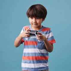 年轻的混合比赛男孩站持有控制台控制器玩视频游戏蓝色的背景有趣的游戏好活动周末