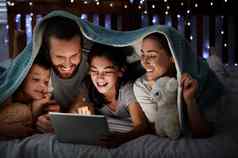 快乐高加索人家庭孩子们数字平板电脑说谎毯子黑暗晚上脸照亮设备屏幕光家庭阅读在线故事看电影睡觉前