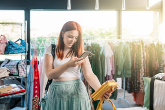 年轻的红发女人快乐购物服装商店采取图片智能手机衣服女孩支出时间购物分享社会网络概念购物