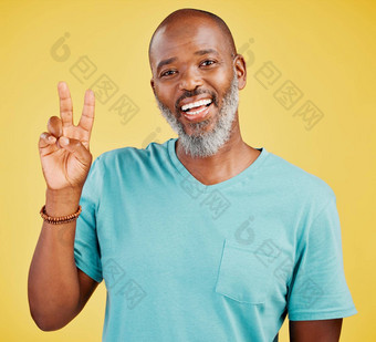 肖像成熟的友好的非洲美国男人。快乐微笑使和平手势手黄色的工作室背景表达完美的显示支持