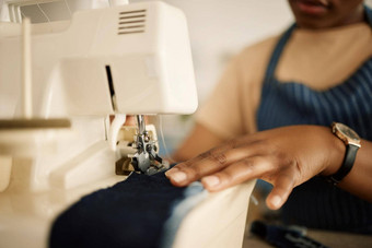 特写镜头手裁缝缝纫机时尚设计师喂养牛仔布缝纫机手裁缝缝合一块材料有创意的女商人工作工作室