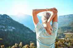 后视图高级女人灰色头发伸展运动手头站在户外俯瞰风景优美的山视图生活健康的活跃的生活方式