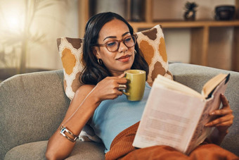 美丽的混合比赛女人阅读书喝咖啡生活房间首页拉美裔说谎休息室沙发享受感觉放松周末小说故事茶