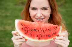 美丽的红发女人微笑牙套吃片西瓜在户外夏天