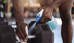 特写镜头未知的非洲美国运动员喷雾瓶抓紧时间哑铃权重健身房活跃的黑色的男人。清洁设备卫生例程保护防止科维德锻炼