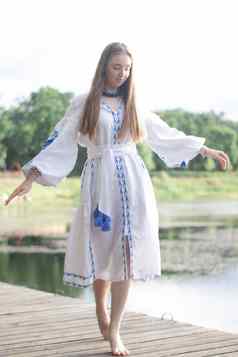 女孩绣花乌克兰衬衫坐在码头反射云水湖海岸天空维希万卡一天自由爱国者