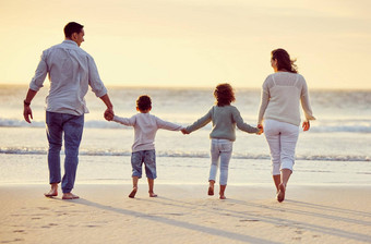 <strong>后</strong>视图拍摄无忧无虑的家庭持有手走海滩日落混合比赛父母孩子们支出时间海享受夏天假期