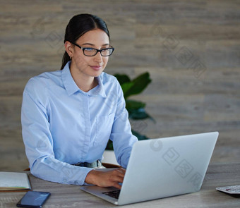 年轻的混合比赛女商人穿眼镜坐着工作移动PC办公室工作快乐拉美裔女人打字电子邮件移动PC工作桌子上工作