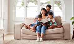 年轻的快乐家庭坐着沙发阅读书首页放松年轻的夫妇阅读书女儿坐着沙发首页