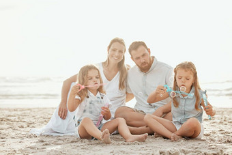 快乐高加索人家庭享受假期海滩年轻的微笑夫妇玩沙子可爱的女儿可爱的姐妹享受夏天一天妈妈爸爸