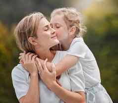 快乐内容年轻的妈妈。拥抱拥抱女儿花园有爱心的女孩站接吻妈妈。脸颊给拥抱公园