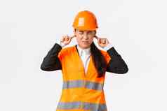 亚洲女公司经理感觉不舒服首席工程师关闭耳朵扮鬼脸烦人的噪音检查工作建设区可怕的声音维修穿安全头盔