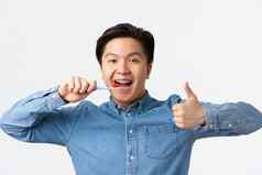 口腔正畸学牙科护理卫生概念特写镜头满意快乐亚洲男人。刷牙牙齿牙套持有牙刷显示竖起大拇指批准白色背景