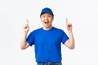 兴奋微笑亚洲年轻的男人。工作快递穿蓝色的统一的帽t恤指出手指乐观的使公告促进提供白色背景