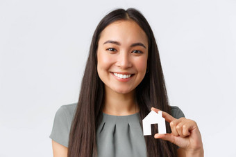 保险贷款真正的房地产家庭概念特写镜头快乐微笑亚洲女人显示小纸房子微型手相机发现完美的公寓白色背景