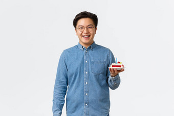 庆祝活动假期生活方式概念微笑英俊的亚洲男人。牙套乐观的持有一块生日蛋糕蜡烛庆祝生日站白色背景