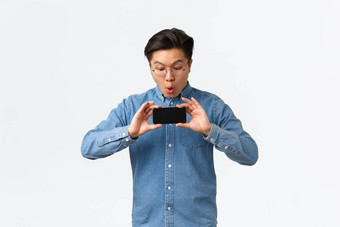 深刻的印象亚洲的家伙反应电影预告片显示朋友移动电话屏幕站在深刻的印象智能手机屏幕惊讶图形游戏站白色背景