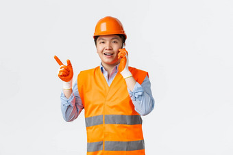 建筑部门工业工人概念微笑亚洲工程师建设经理<strong>反光衣</strong>物头盔指出手指左会说话的移动电话白色背景