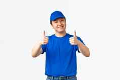 友好的微笑亚洲交付的家伙蓝色的统一的帽t恤显示竖起大拇指批准推荐保证确保包裹好安全白色背景
