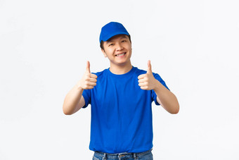 友好的微笑亚洲交付的家伙蓝色的统一的帽t恤显示竖起大拇指批准推荐保证确保包裹好安全白色背景