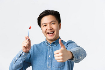 口腔正畸学牙科护理卫生概念特写镜头满意快乐亚洲的家伙持有牙刷微笑牙齿牙套显示竖起大拇指批准白色背景