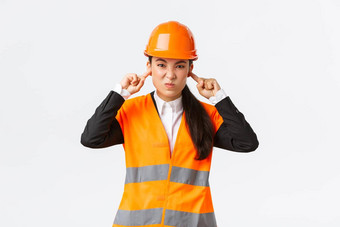 困扰不高兴亚洲女首席工程师关闭耳朵扮鬼脸可怕的大声噪音建设区域穿安全头盔抱怨困扰声音白色背景