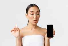 美个人亲密的护理移动应用程序概念漂亮的亚洲女人浴毛巾持有止血栓显示智能手机屏幕月经周期跟踪器期流应用程序