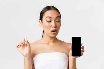 美个人亲密的护理移动应用程序概念漂亮的亚洲女人浴毛巾持有止血栓显示智能手机屏幕<strong>月经周期</strong>跟踪器期流应用程序