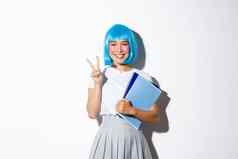 美丽的亚洲女孩蓝色的动漫假发显示卡哇伊和平手势持有笔记本电脑穿女学生服装万圣节聚会，派对