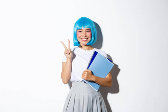 美丽的亚洲女孩蓝色的动漫假发显示卡哇伊和平手势持有笔记本电脑穿女<strong>学生服装</strong>万圣节聚会，派对