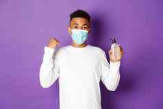 概念科维德流感大流行社会距离图像快乐非裔美国人男人。医疗面具显示手洗手液拳头泵欢乐站紫色的背景