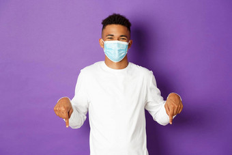 概念冠状病毒检疫生活方式英俊的非裔美国人的家伙医疗面具显示促销指出手指标志微笑站紫色的背景