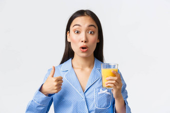 健康的生活方式早....例程人概念特写镜头惊讶满意亚洲女孩惊讶显示竖起大拇指新鲜的橙色汁白色背景