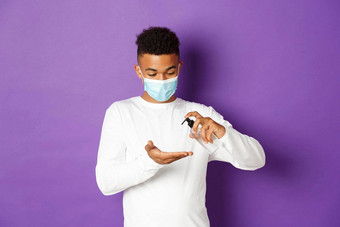 概念科维德流感大流行社会距离图像年轻的非裔美国人的家伙手洗手液穿医疗<strong>面具</strong>白色运动衫站<strong>紫色</strong>的背景