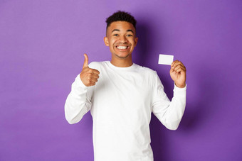 肖像惊讶非裔美国人男人。显示竖起大拇指信贷卡推荐银行贷款站紫色的背景