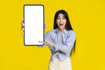 大智能手机手美丽的亚洲女孩白色屏幕快乐介绍应用<strong>程序游戏</strong>赢得孤立的黄色的背景移动应用<strong>程序</strong>广告产品放置