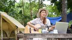 快乐的年轻的女旅行者玩吉他野营溪夏天假期