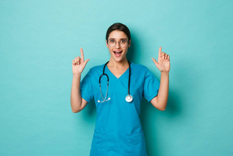 冠状病毒流感大流行社会距离概念图像兴奋美丽的医生穿实习医生风云眼镜指出手指复制空间微笑逗乐站蓝色的背景