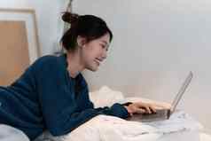 年轻的美丽的亚洲女人购物在线移动PC连接无线网络网络女人工作移动PC床上