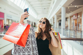 快乐年轻的美丽的女人调用视频电话显示购物袋