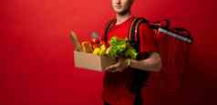作物图片交付男人。红色的统一的携带纸盒子食物产品孤立的红色的背景食物交付服务