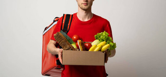 作物图片交付男人。红色的t恤携带纸盒子水果蔬菜孤立的白色背景食物交付服务