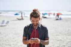 快乐年轻的男人。智能手机海滩享受阳光明媚的一天听音乐穿耳机