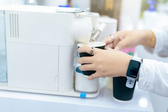 女人使杯热咖啡胶囊咖啡机女人持有黑色的杯采取咖啡胶囊咖啡机表格表示制造商早....喝现代首页设备