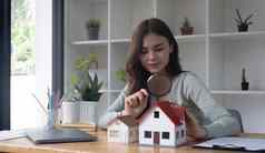 快乐女人手持有放大玻璃房子模型房子选择真正的房地产概念