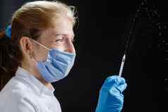 医生喷雾注射器黑色的背景医生微笑保护面具药物注射器倒空气女人医生穿医疗面具手套鞘液体大注射器蓝色的背景