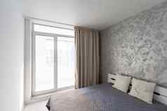 时尚的室内当代卧室舒适的家具床上毯子枕头镜子盆栽植物灰色的墙背景现代首页窗帘太阳耀斑