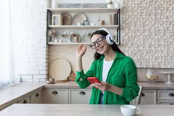 美丽的年轻的女人眼镜绿色衬衫放松首页厨房听音乐